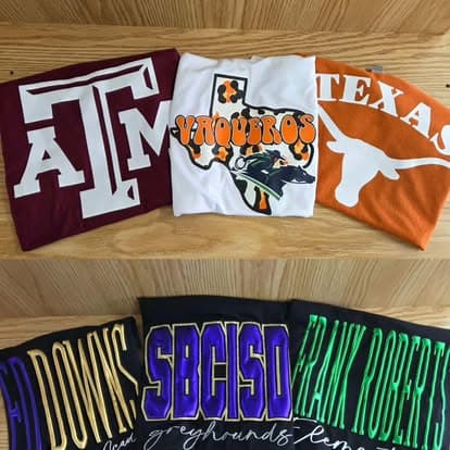 Three Texas A&M tees on a wood table.